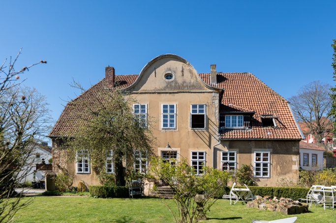Gelbes Haus mit Satteldach und Garten, blauer Himmel im Hintergrund.