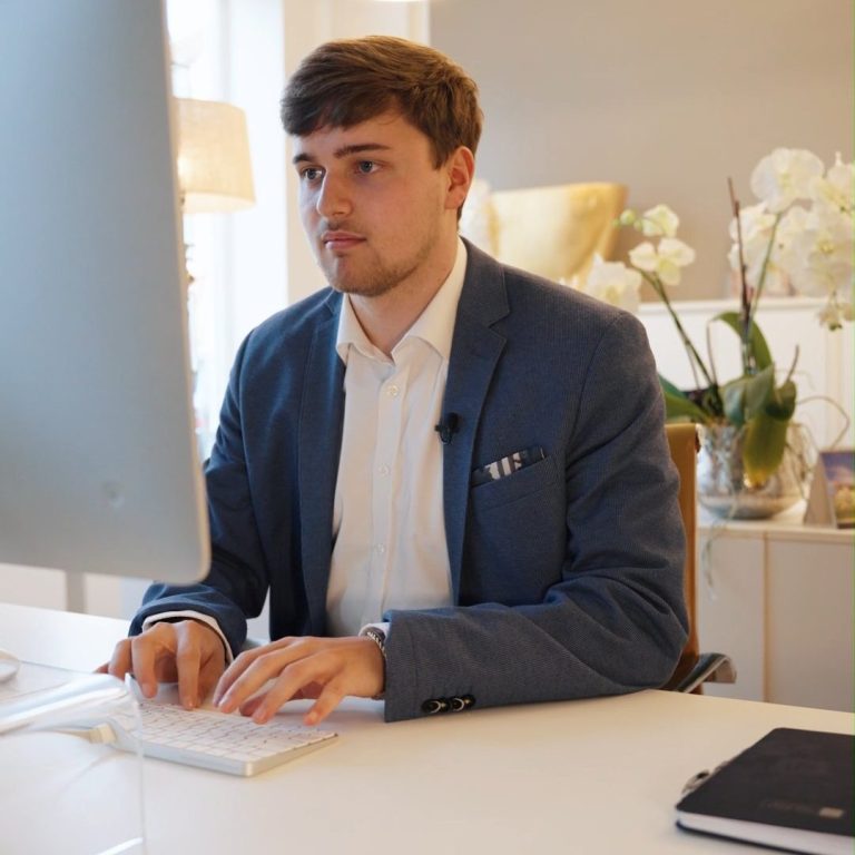 Mann in Anzug sitzt am Schreibtisch und arbeitet am Computer. Orchideen im Hintergrund.