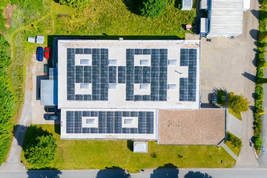 Dachansicht eines Gebäudes mit Solarpanelen und umliegendem Grün.