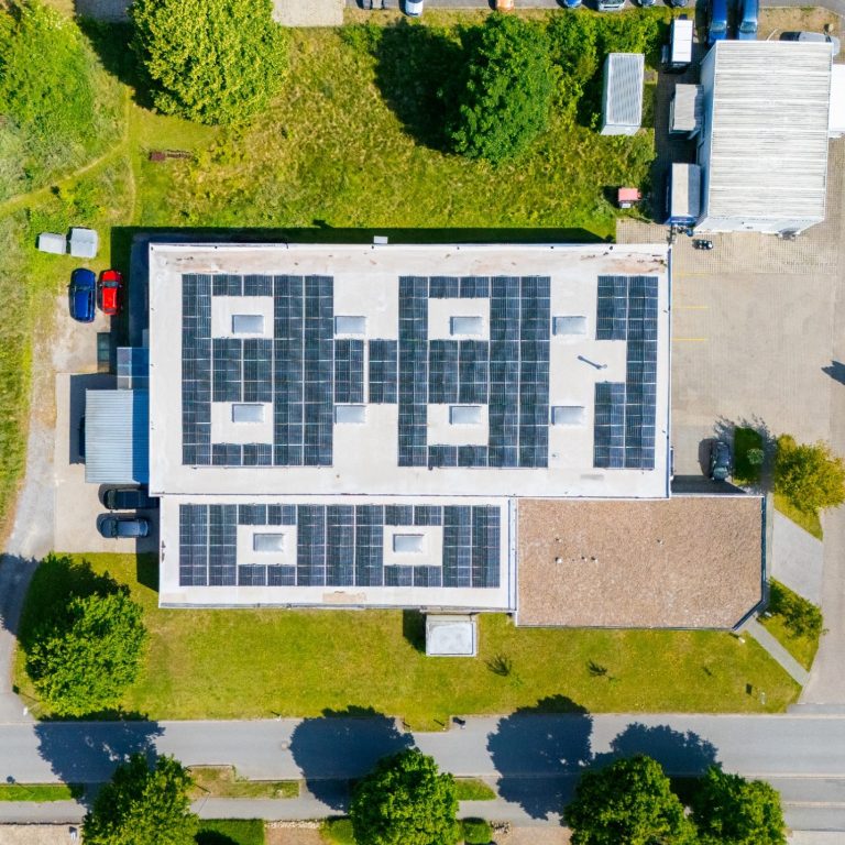 Dachansicht eines Gebäudes mit Solarpanels und umgebendem Grün.