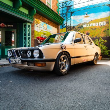 Ein beige-farbener klassischer BMW, geparkt vor einer farbenfrohen Wand mit Hollywood-Motiv.
