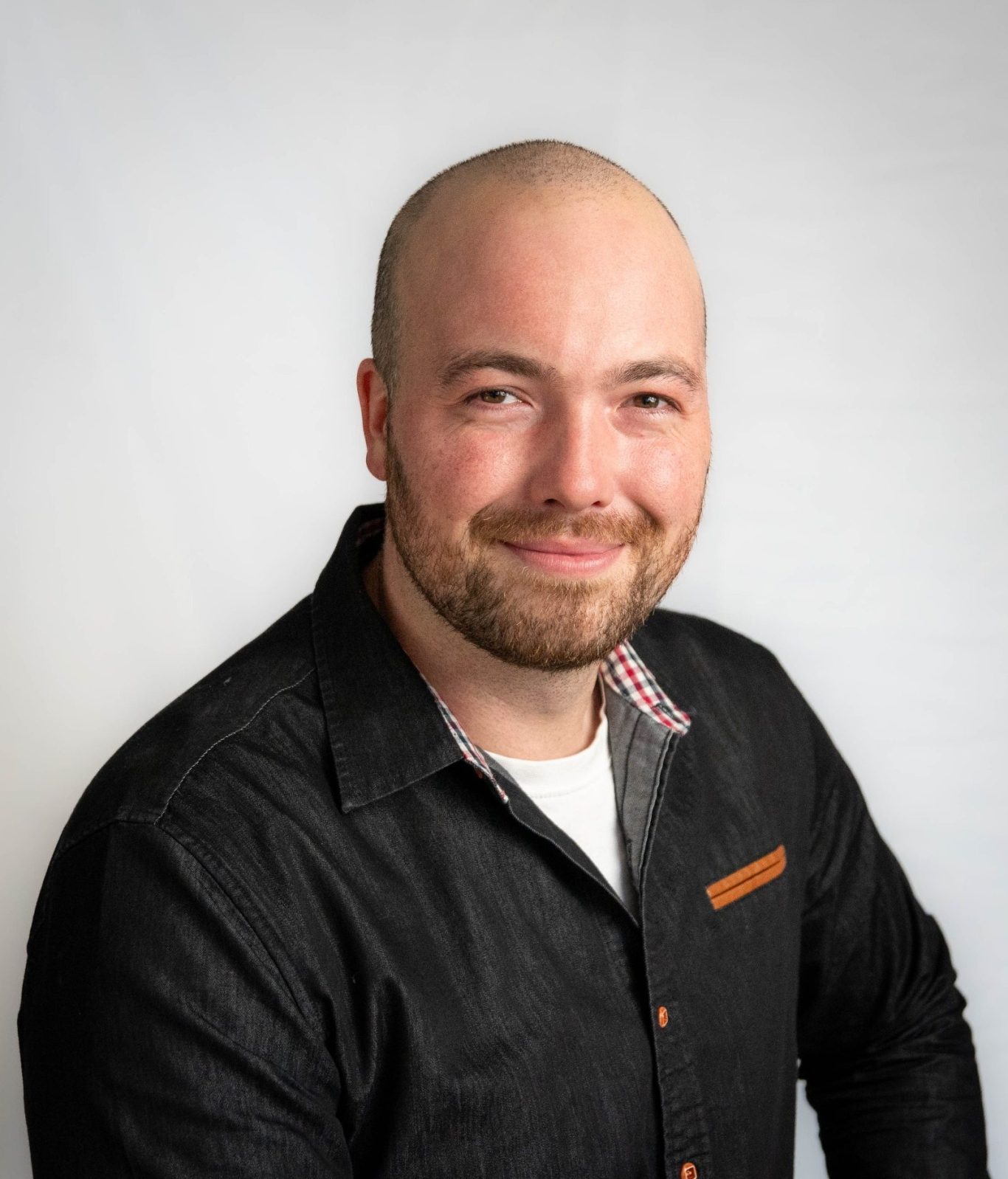 Mann mit Glatze und kurzem Bart, trägt ein schwarzes Hemd und lächelt freundlich.