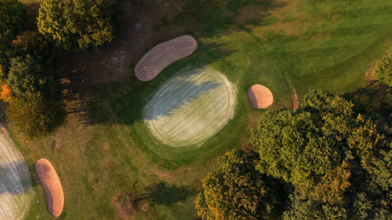 Luftaufnahme eines Golfplatzes mit Sandbunkern und umgeben von Bäumen.