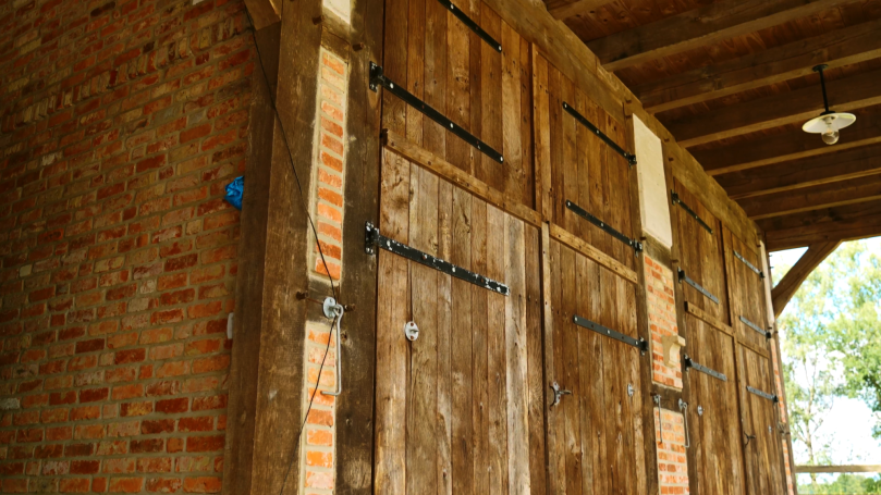 Holztür mit Metallbeschlägen und roten Ziegeln in einer rustikalen Umgebung.