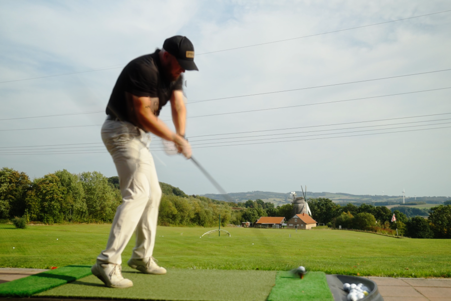 Mann beim Golfspiel auf einer Driving Range mit Aussicht auf die Landschaft.