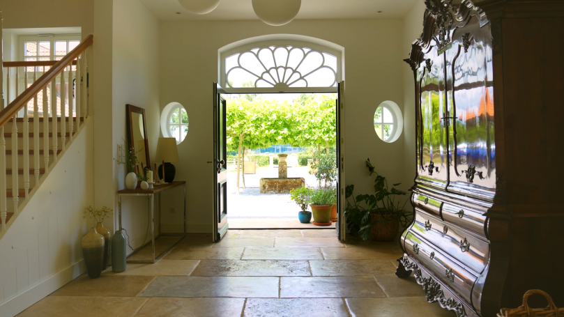 Heller Eingangsbereich mit einer offenen Tür, Pflanzen und einem großen Holzschrank.