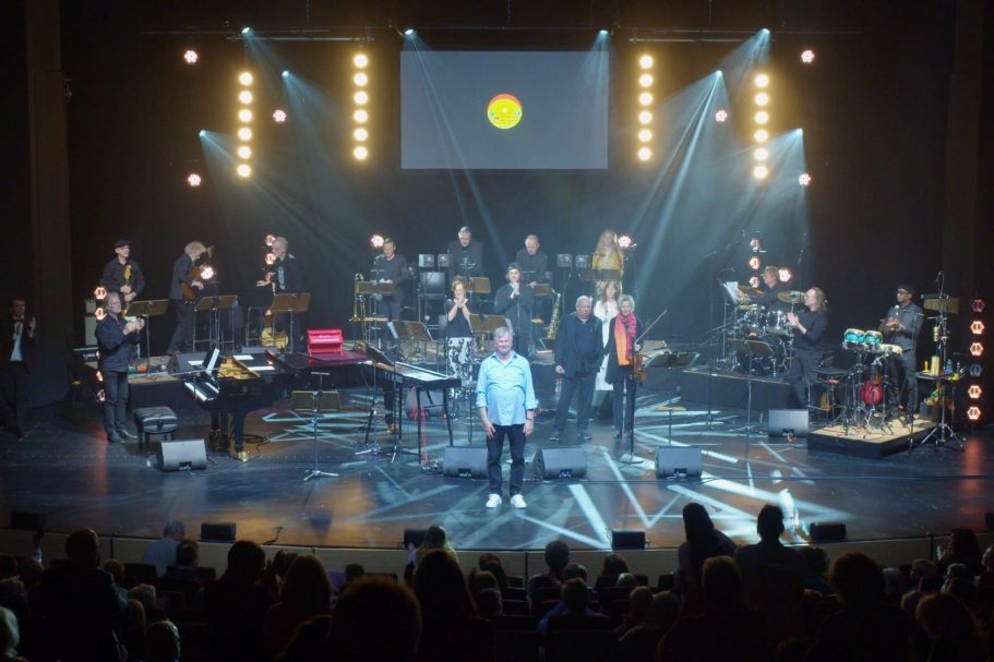 Live-Bühne mit Musikern, Lichtern und einem Hauptsänger im Vordergrund.