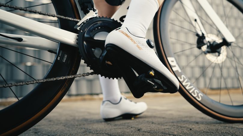 Nahaufnahme eines Fußes in einem Radschuh, der auf ein Fahrradpedal drückt.