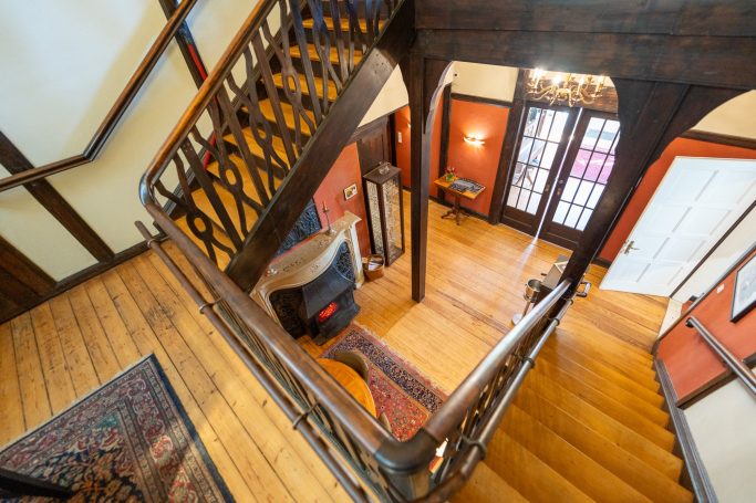 Holztreppe mit gelben Wänden und bunten Teppichen in einer stilvollen Eingangshalle.