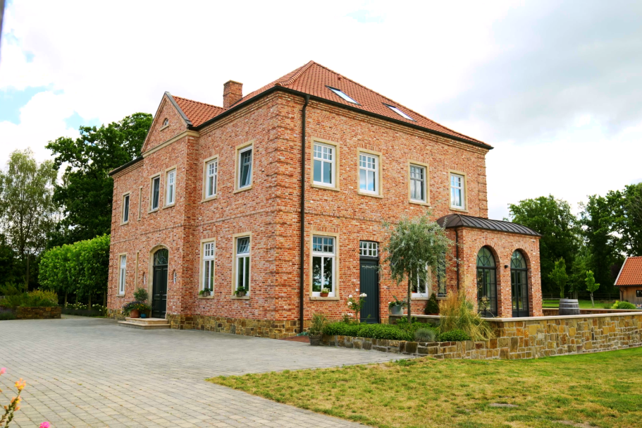 Zweistöckiges, rotes Backsteinhaus mit Garten und verglaster Veranda.