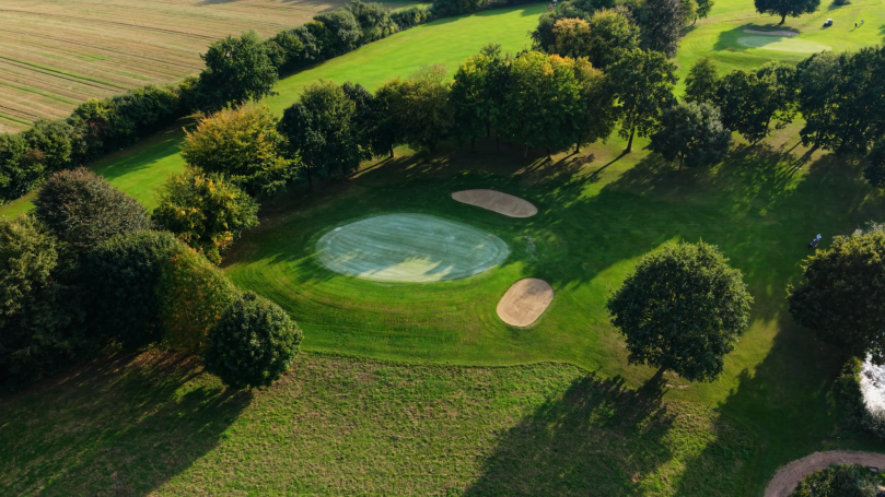 Golfplatz mit einem grünen Fairway, zwei Sandbunkern und umgebenden Bäumen.