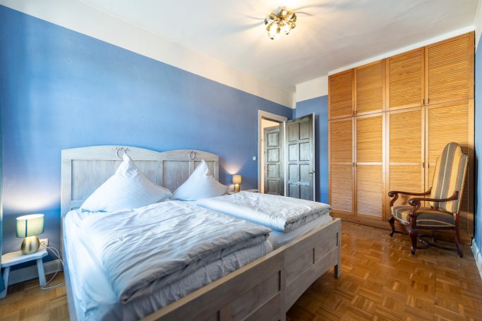 Geräumiges Schlafzimmer mit blauem Anstrich, Doppelbett und schlichter Holzmöbel.